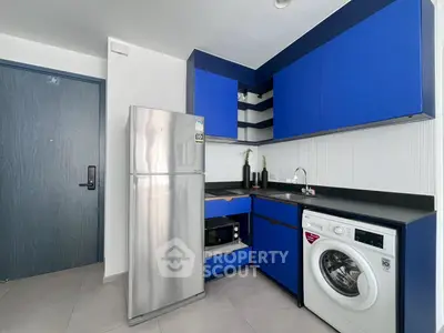 Modern kitchen with blue cabinets, stainless steel fridge, and washing machine.