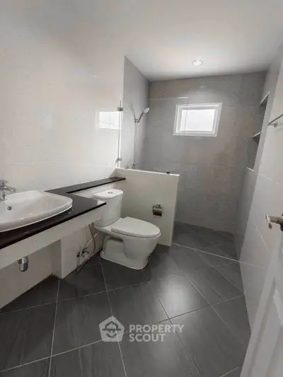Modern bathroom with sleek design and tiled flooring, featuring a shower and contemporary fixtures.