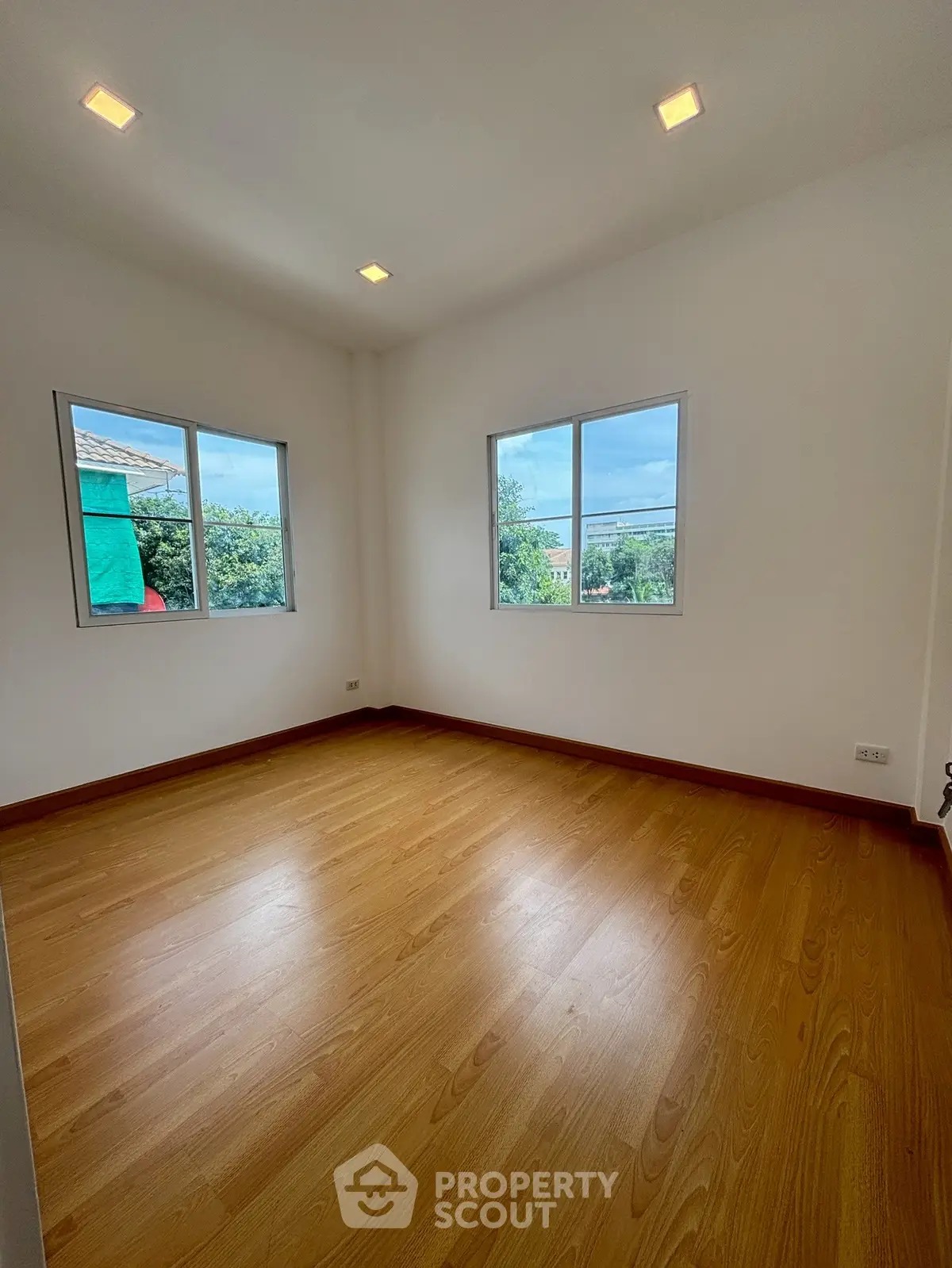 Spacious empty room with wooden flooring and large windows offering natural light.
