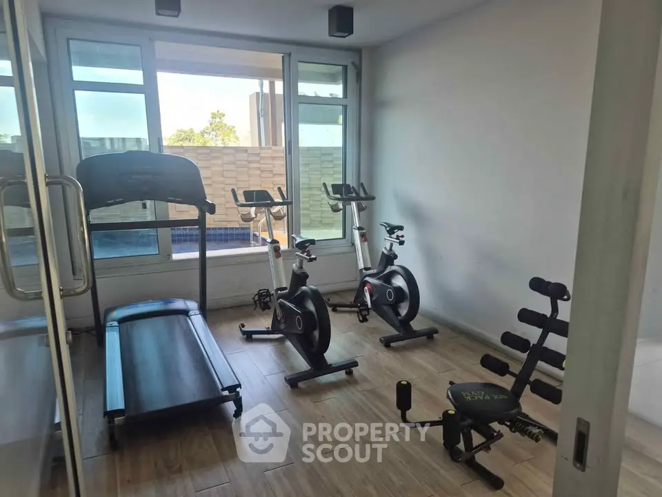 Modern gym with treadmill and exercise bikes in a bright, spacious room with large windows.