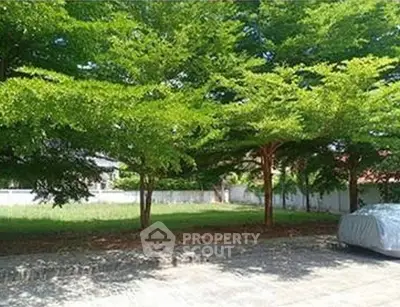 Spacious garden area with lush trees and a covered car, perfect for outdoor relaxation.