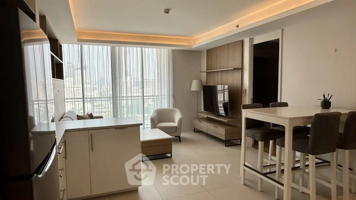 Modern living room with open kitchen and city view, featuring sleek furniture and ambient lighting.