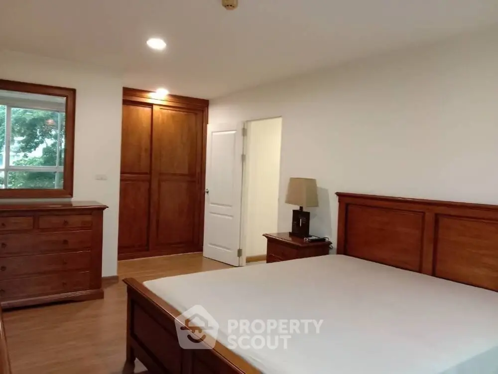 Spacious bedroom with wooden furniture and large window offering natural light.