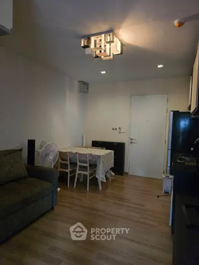 Cozy living room with modern lighting and dining area, featuring wooden flooring and a compact kitchen.