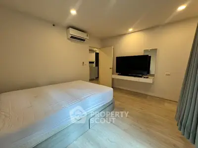 Modern bedroom with minimalist design, featuring a large bed, wall-mounted TV, and air conditioning.