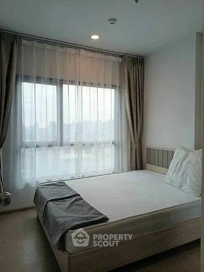 Cozy bedroom with large window and modern decor in urban apartment.