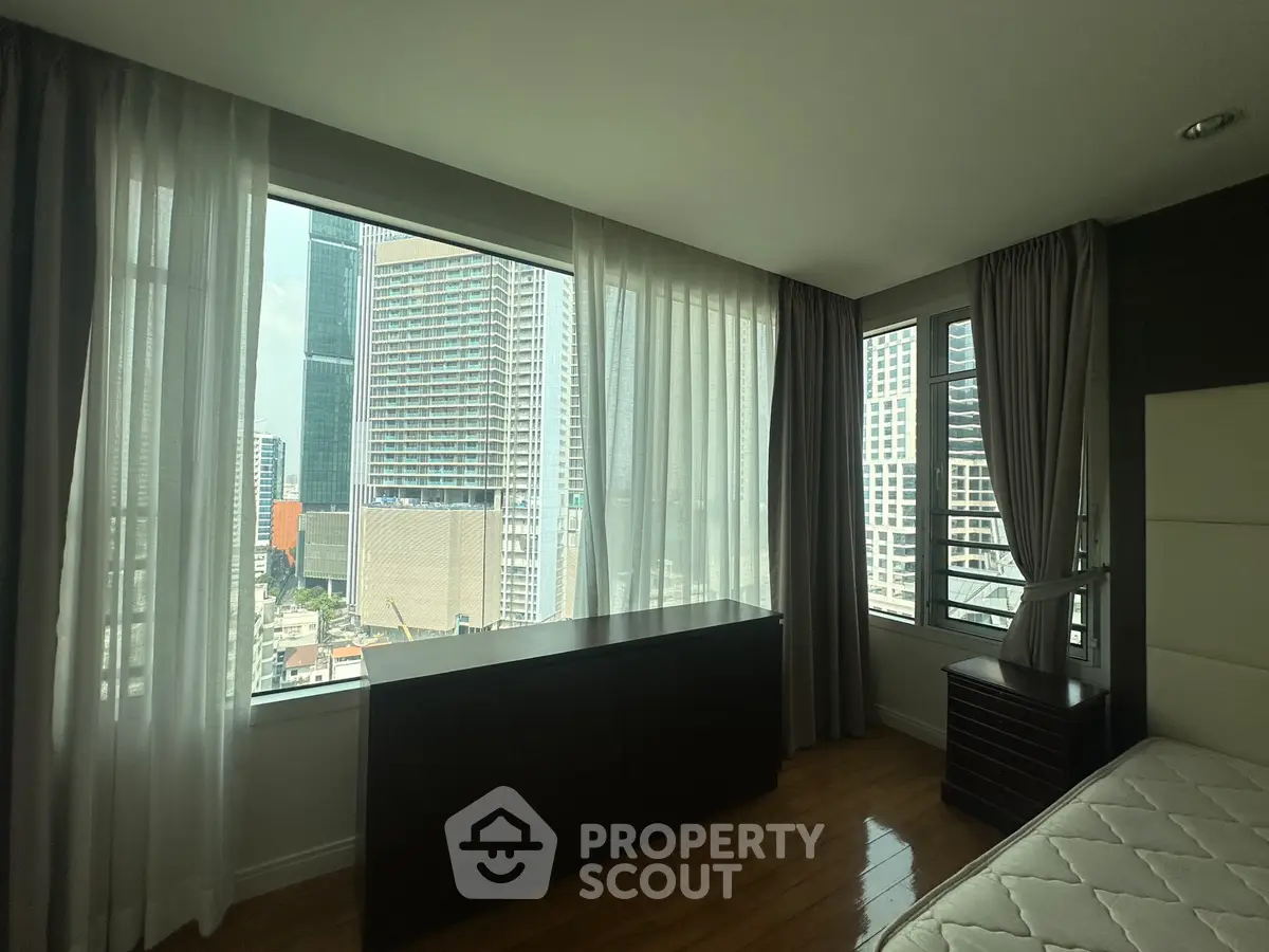 Spacious bedroom with large windows offering stunning city views in a modern high-rise building.