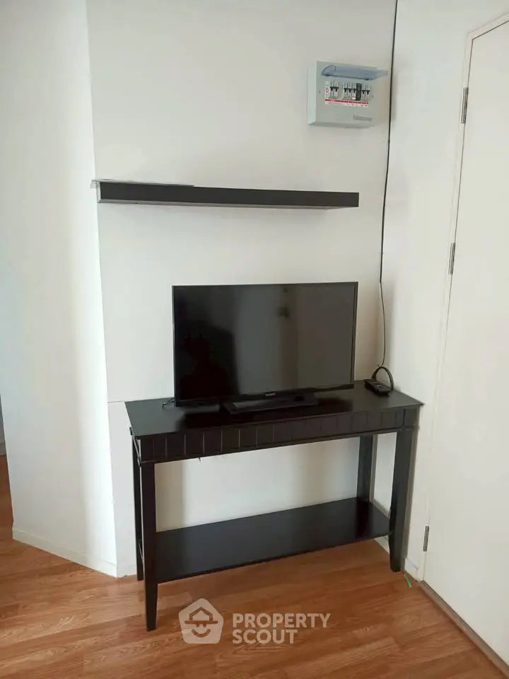 Modern living room with sleek black TV stand and wall-mounted shelf, showcasing minimalist design.