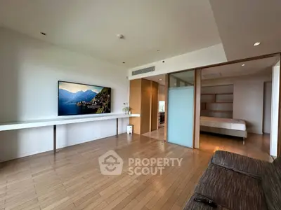 Spacious modern living room with wooden flooring and large TV, adjacent to a cozy bedroom.
