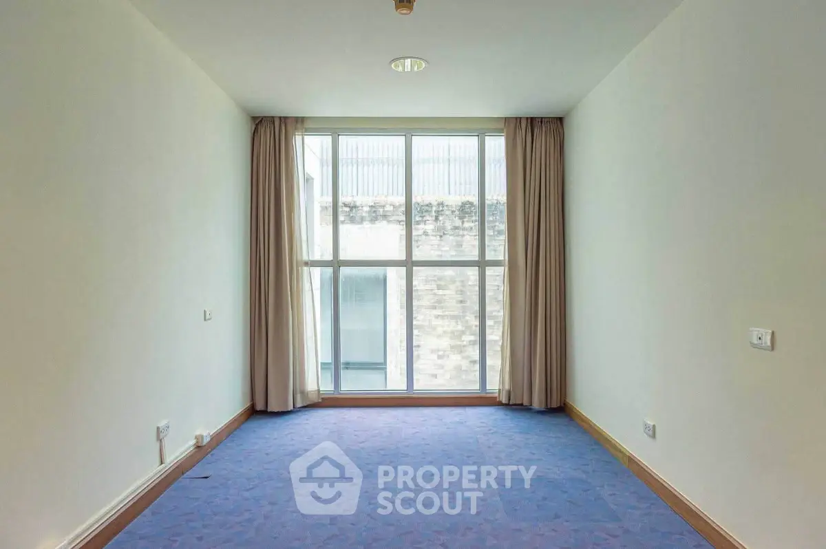 Spacious empty room with large window and blue carpet, ideal for customization.