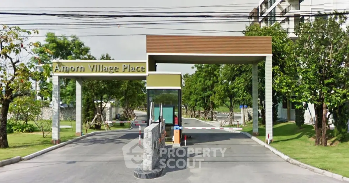 Amorn Village Place entrance with modern design and lush greenery, showcasing a welcoming residential community.