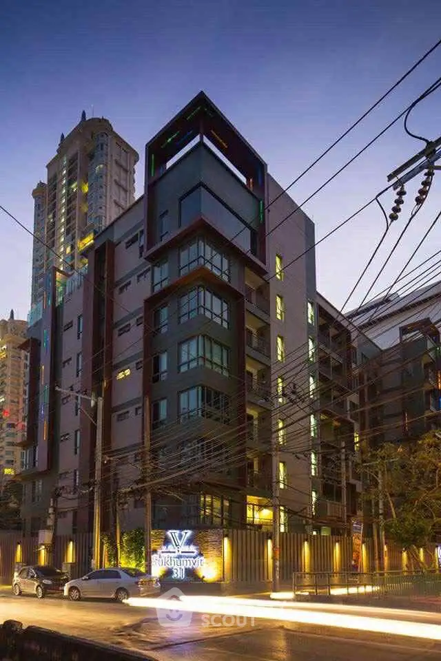 Modern urban apartment building with contemporary design and illuminated signage at dusk.