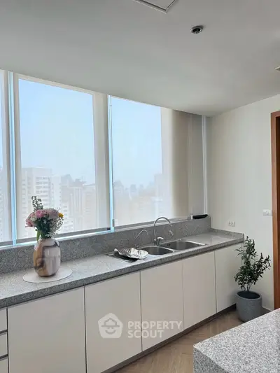 Modern kitchen with large windows and sleek countertops in a high-rise apartment.