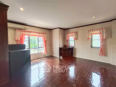 Spacious room with wooden flooring and large windows, perfect for versatile living space.