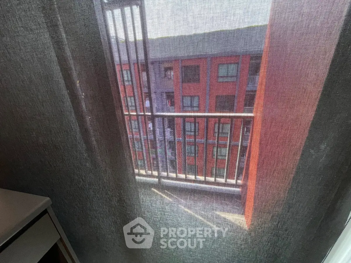 View through a sheer curtain of a modern apartment building with balcony.