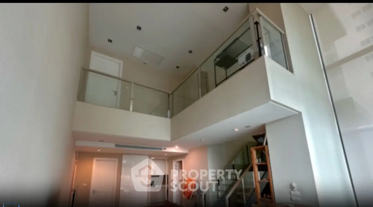 Modern duplex apartment with high ceilings and glass balcony, featuring a sleek staircase and open layout.