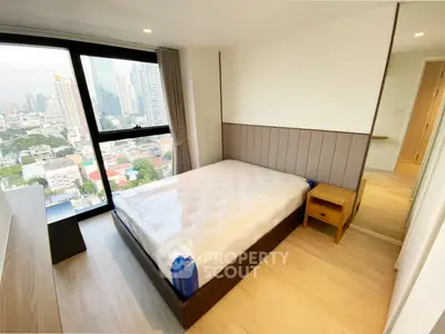 Modern bedroom with city view, featuring a large window and stylish decor in a high-rise apartment.