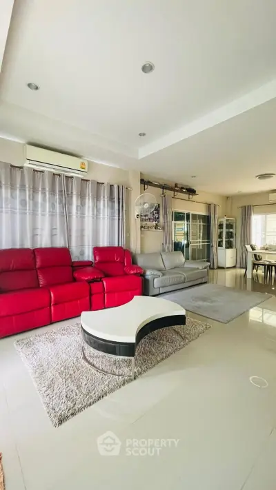 Spacious living room with modern red and gray sofas, elegant coffee table, and bright natural lighting.