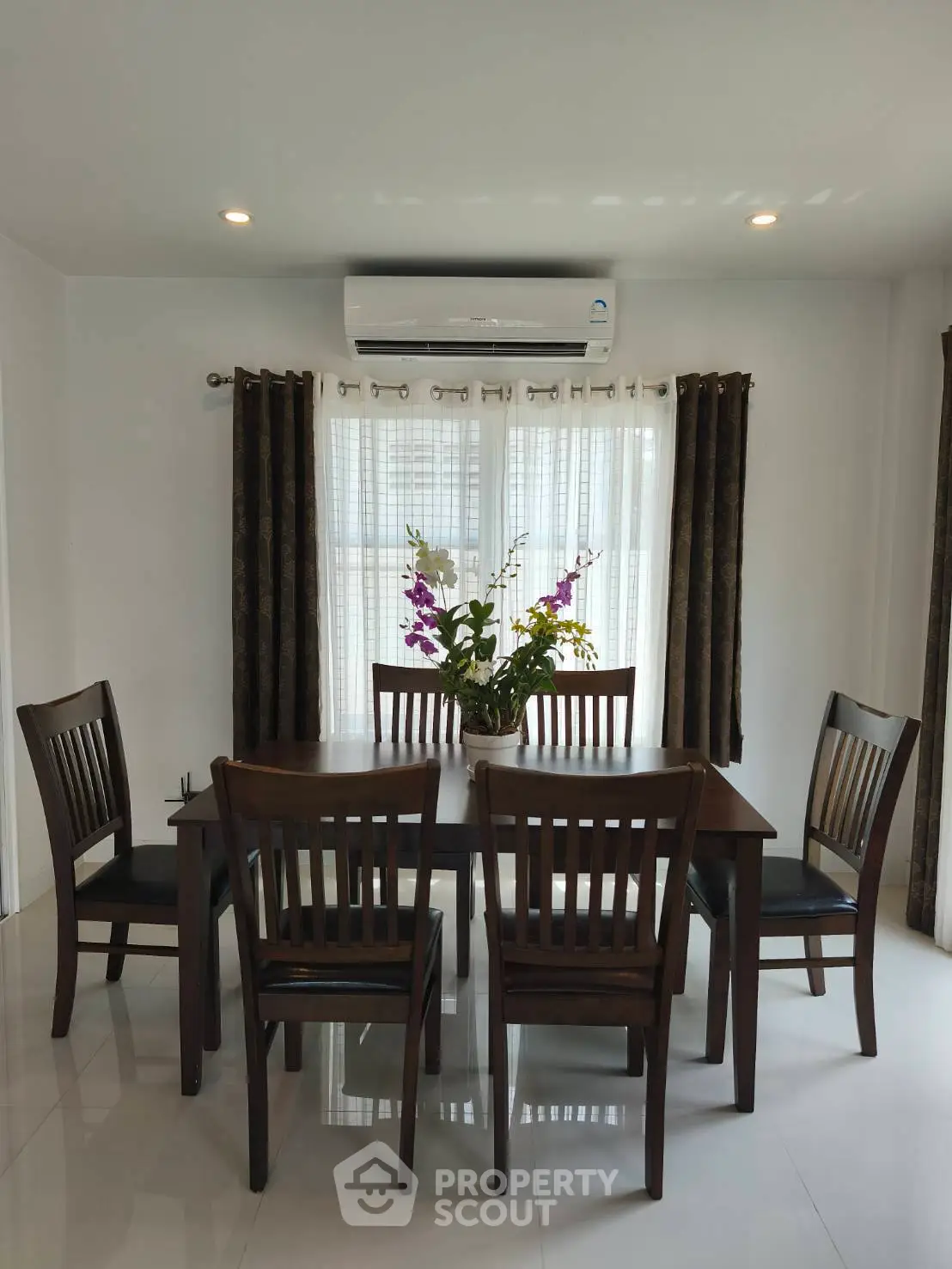 Elegant dining area with wooden table and chairs, featuring a floral centerpiece and natural light from large windows.