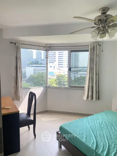 Bright bedroom with city view, featuring a ceiling fan and modern furnishings.