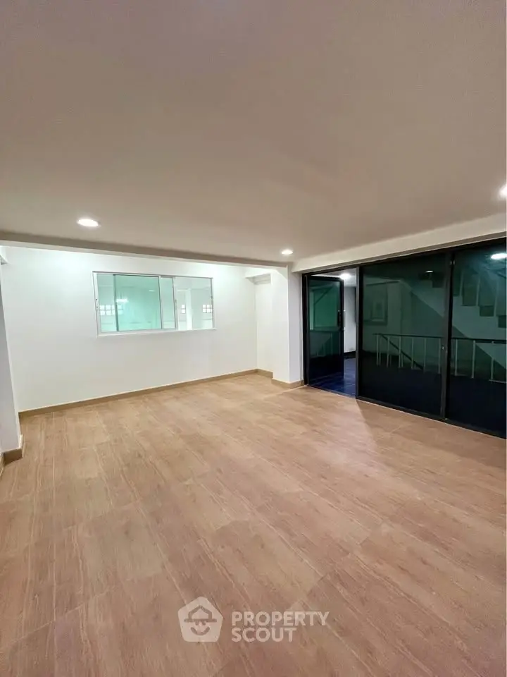 Spacious empty room with wooden flooring and large glass doors leading to a balcony, ideal for customization.