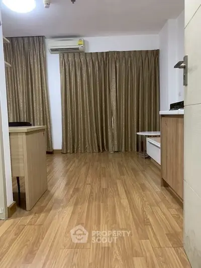 Spacious living room with wooden flooring and elegant curtains, featuring modern air conditioning.