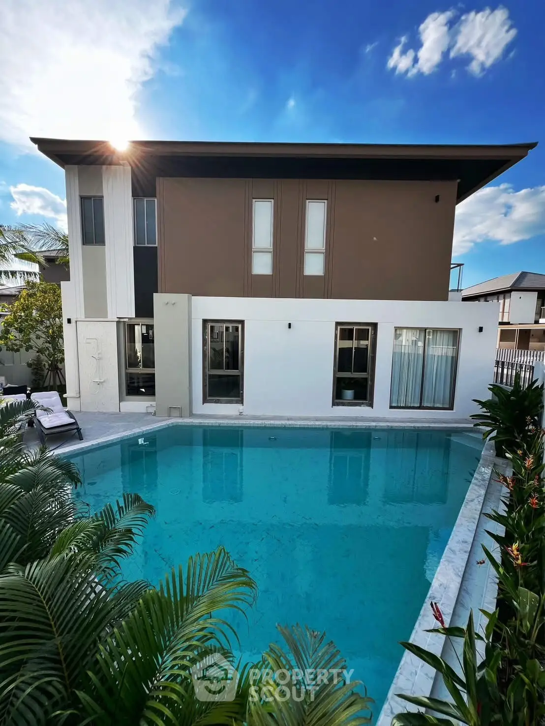 Modern two-story house with a stunning pool and lush greenery under a clear blue sky.