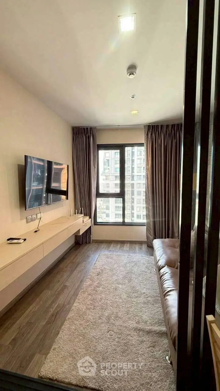 Modern living room with large window and wall-mounted TV in urban apartment.