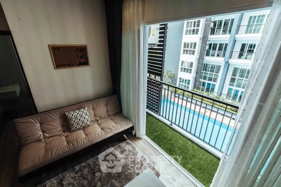 Modern living room with balcony overlooking pool in luxury apartment complex.