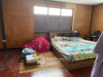 Cozy bedroom with wooden walls and large window, featuring a comfortable bed and luggage storage.
