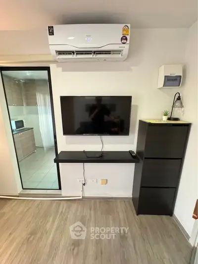 Modern living room with wall-mounted TV and air conditioning, featuring sleek storage and open kitchen view.