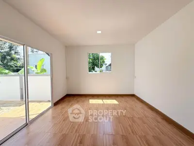 Spacious sunlit room with wooden flooring and large windows, perfect for versatile living space.