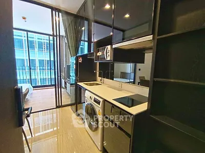 Modern kitchen with sleek appliances and open layout leading to a bright living area with balcony view.