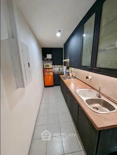 Compact kitchen with sleek dark cabinets and modern appliances in a narrow layout.