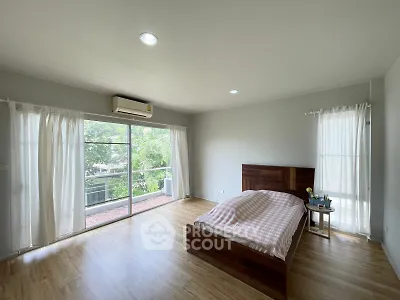 Spacious bedroom with large windows and balcony access, featuring wooden flooring and modern decor.
