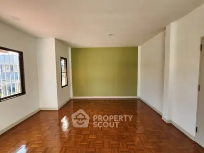 Spacious empty room with wooden flooring and green accent wall, perfect for customization.