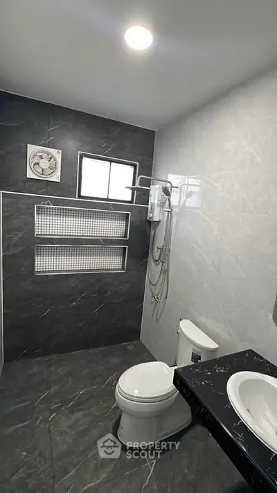Modern bathroom with sleek black and white tiles, featuring a shower and toilet.