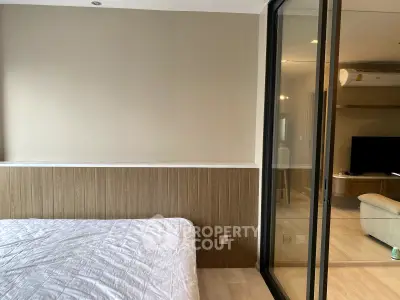 Modern bedroom with sliding glass doors leading to a cozy living room, featuring neutral tones and sleek design.