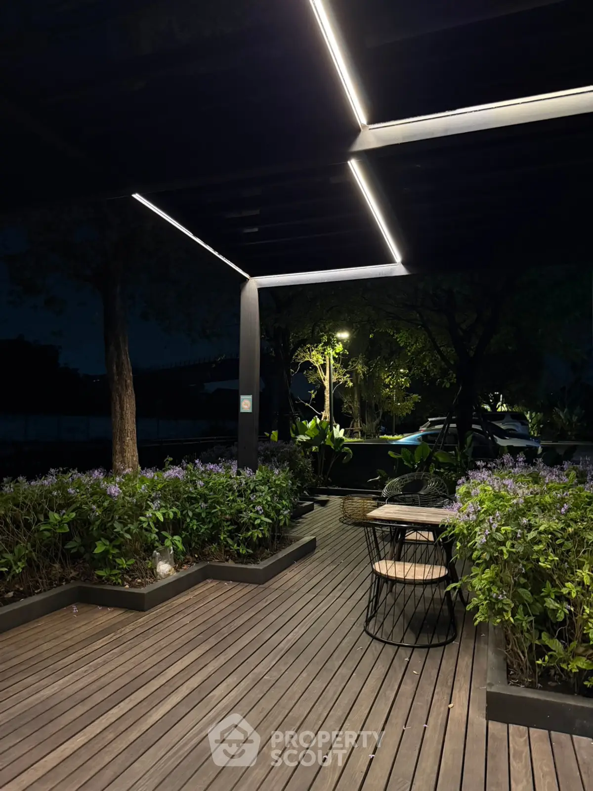 Charming outdoor patio with modern lighting and lush greenery, perfect for evening relaxation.