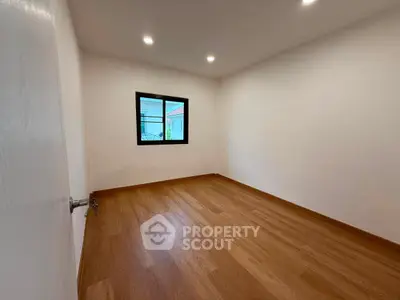 Spacious empty room with wooden flooring and large window, perfect for customization.