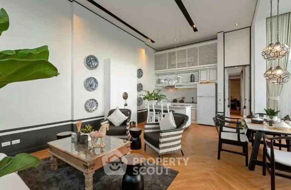 Stylish open-layout living room with modern decor and kitchen area, featuring elegant lighting and wooden flooring.