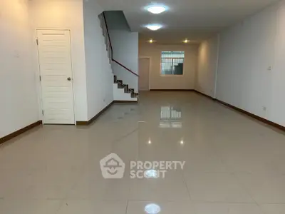 Spacious empty living room with glossy tiled floors and staircase, perfect for customization.
