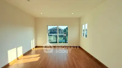 Spacious empty room with wooden flooring and large windows offering natural light and scenic view.