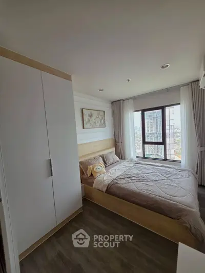 Modern bedroom with large window offering city view, featuring cozy bed and stylish decor.