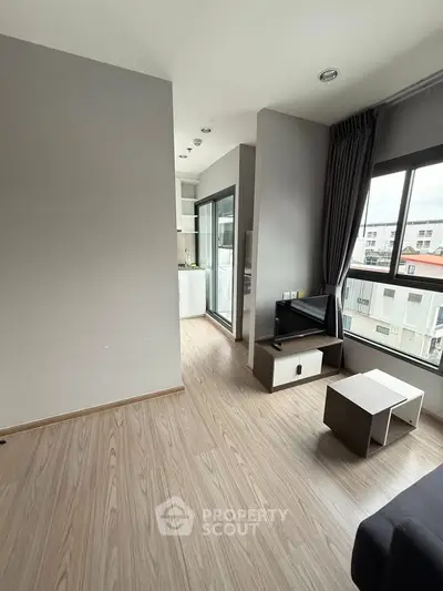 Modern living room with wooden flooring and large windows offering city views.