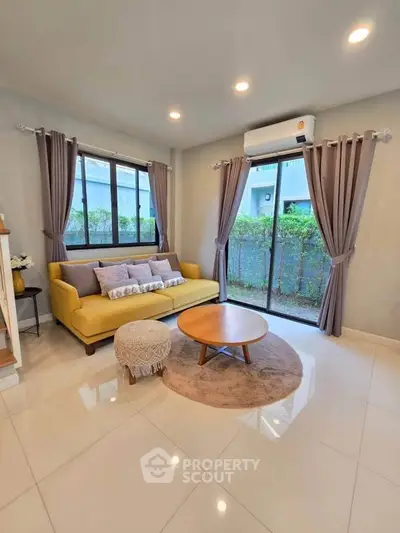 Modern living room with yellow sofa, stylish decor, and large windows offering natural light.
