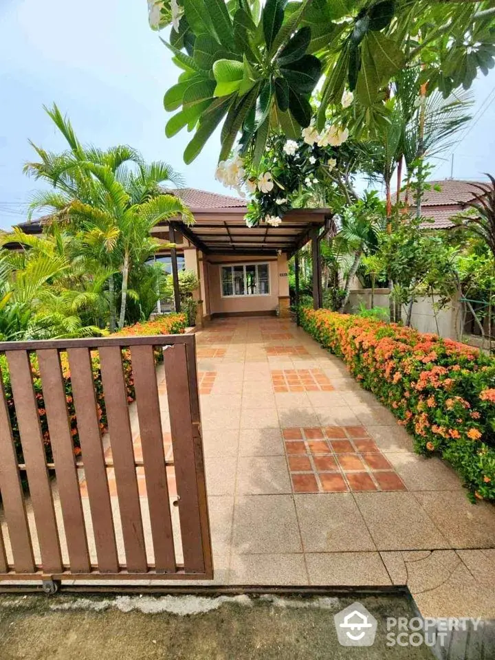 Charming garden entrance with lush greenery and tiled pathway leading to a cozy home.