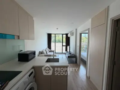 Modern apartment interior with open kitchen and cozy living room, featuring large windows and natural light.