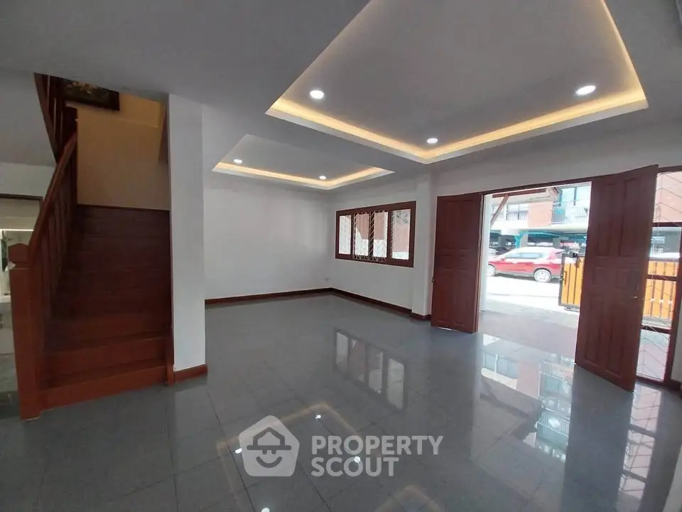 Spacious living room with modern lighting and wooden accents, featuring large windows and open layout.