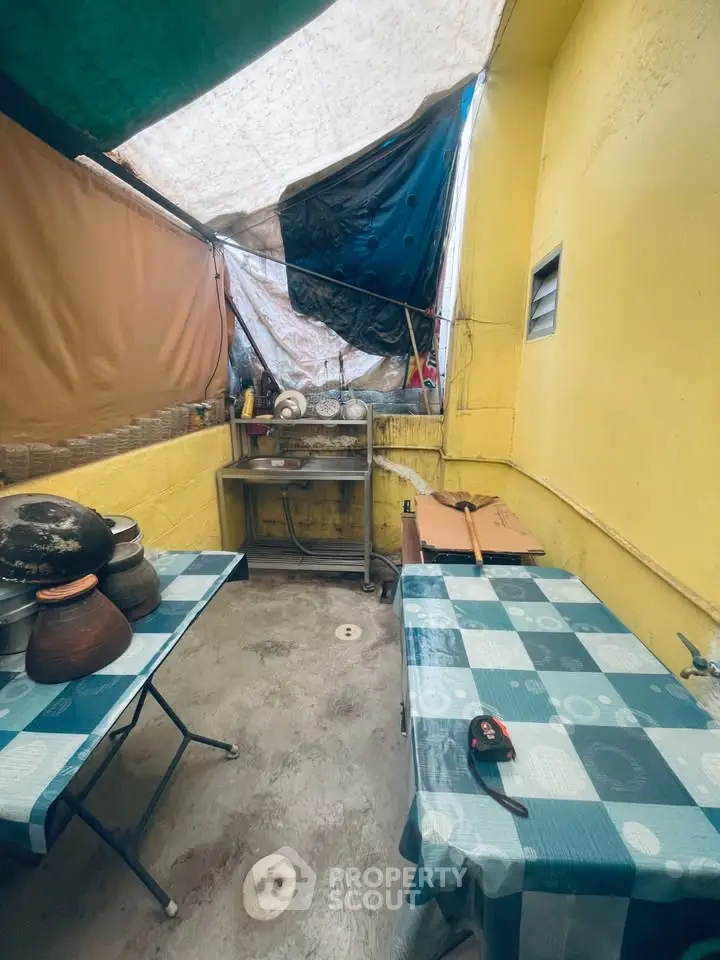 Cozy outdoor kitchen area with vibrant yellow walls and blue checkered tablecloths, perfect for casual dining.